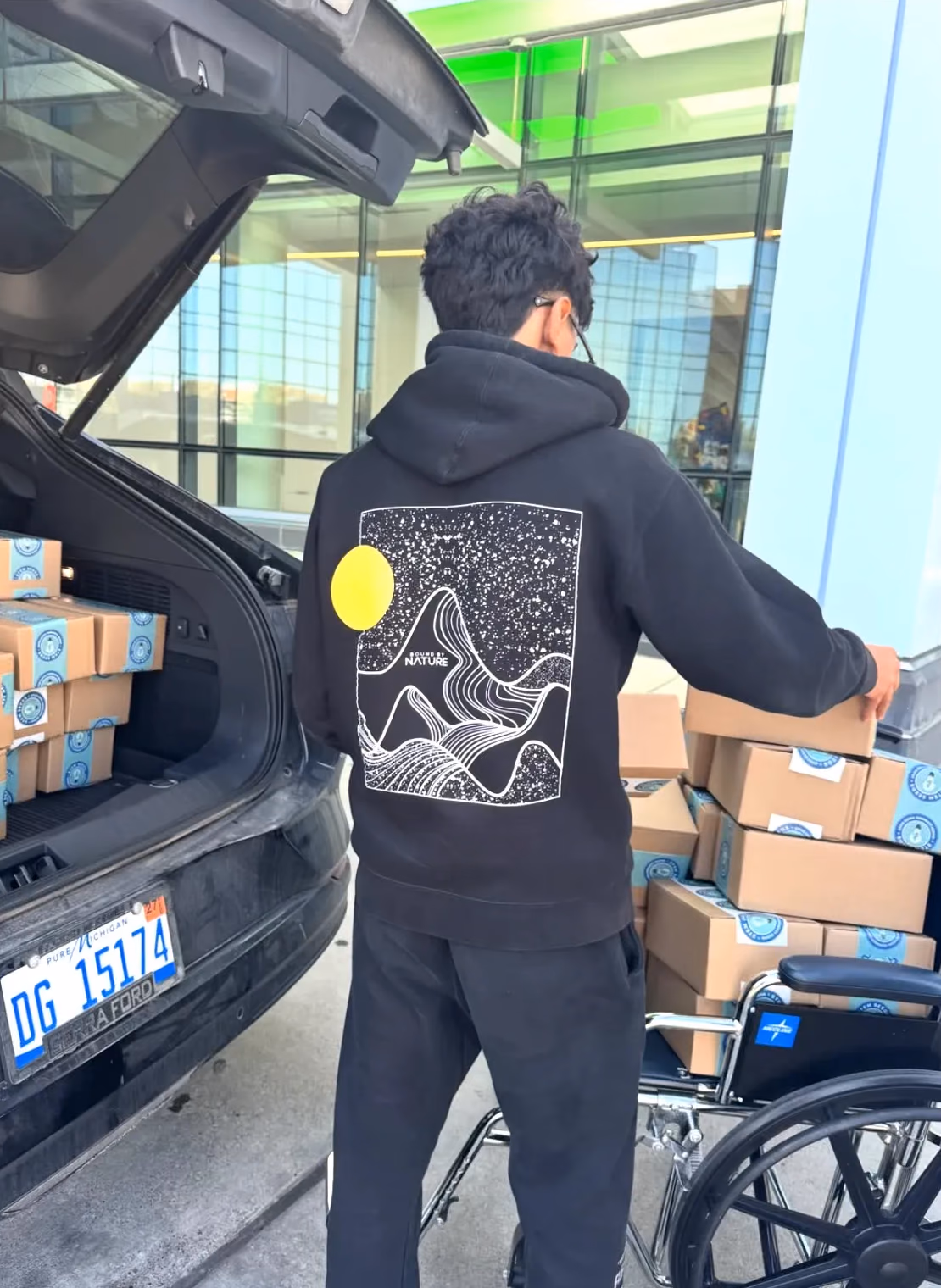 A chapter member stacking STEMKit boxes onto a wheelchair outside the Children's Hospital of Michigan