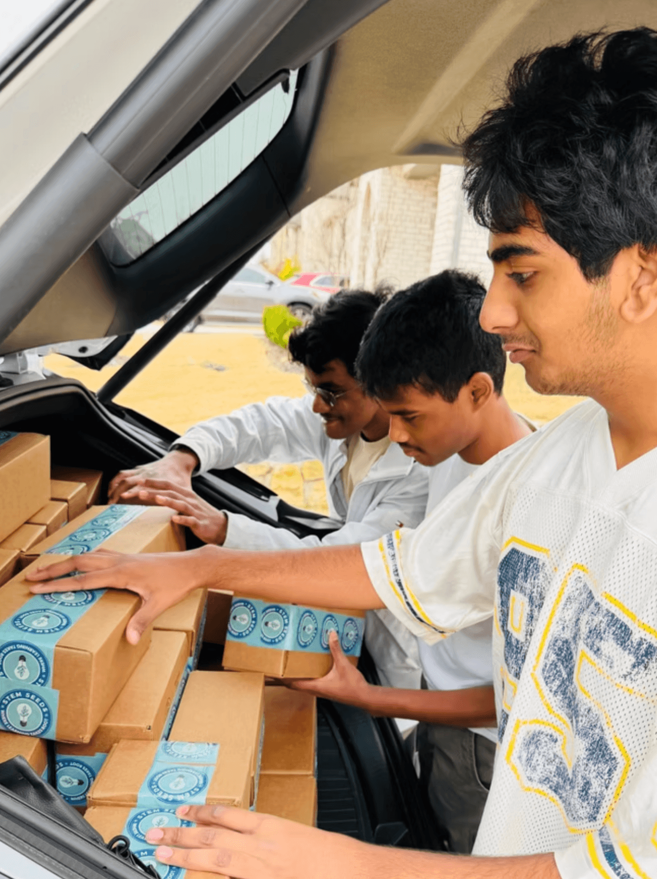 Students loading STEM kits from the back of a car