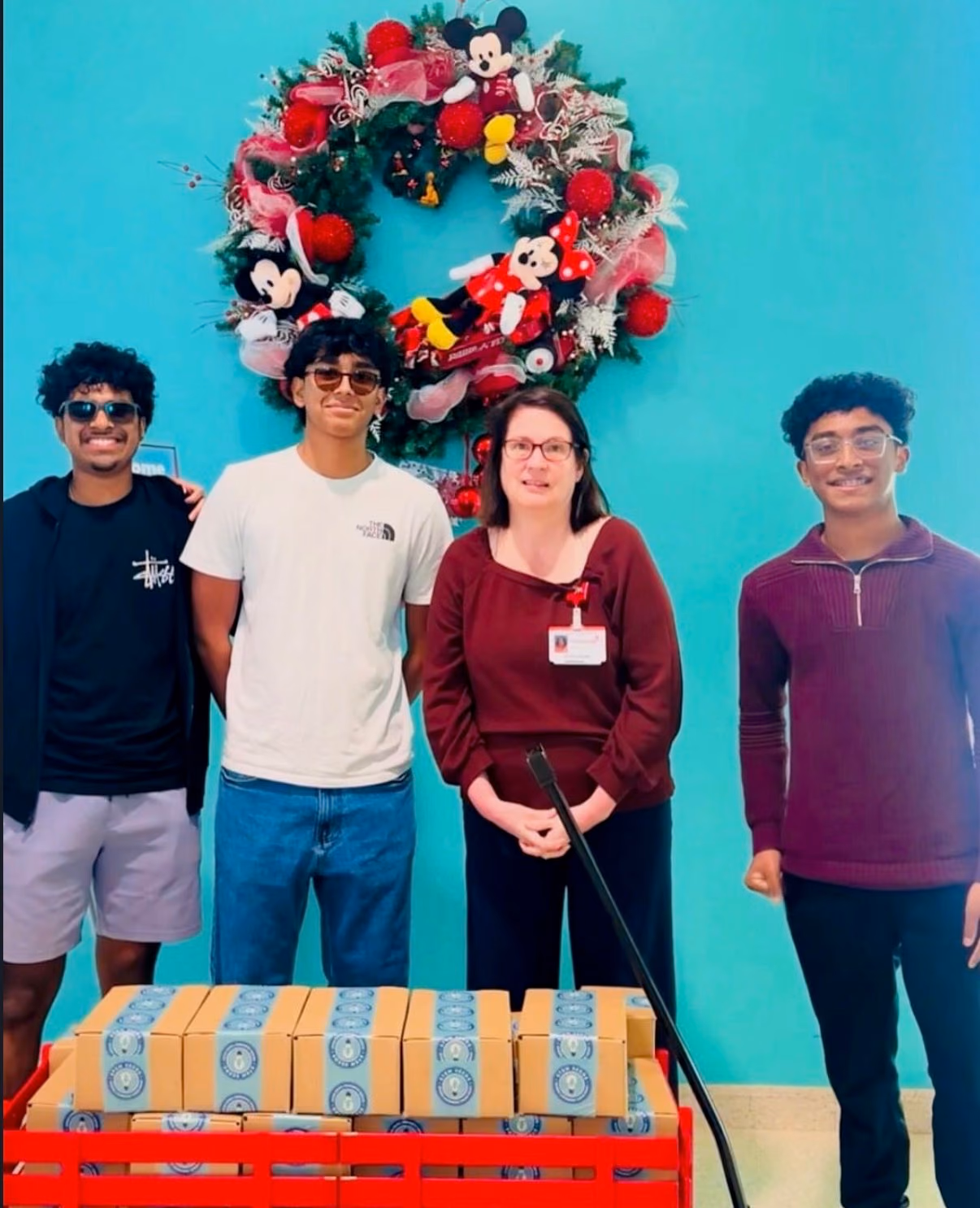 Three STEMSeeds members and a Children's Health staff member beside a wagon of STEMKits under a holiday wreath