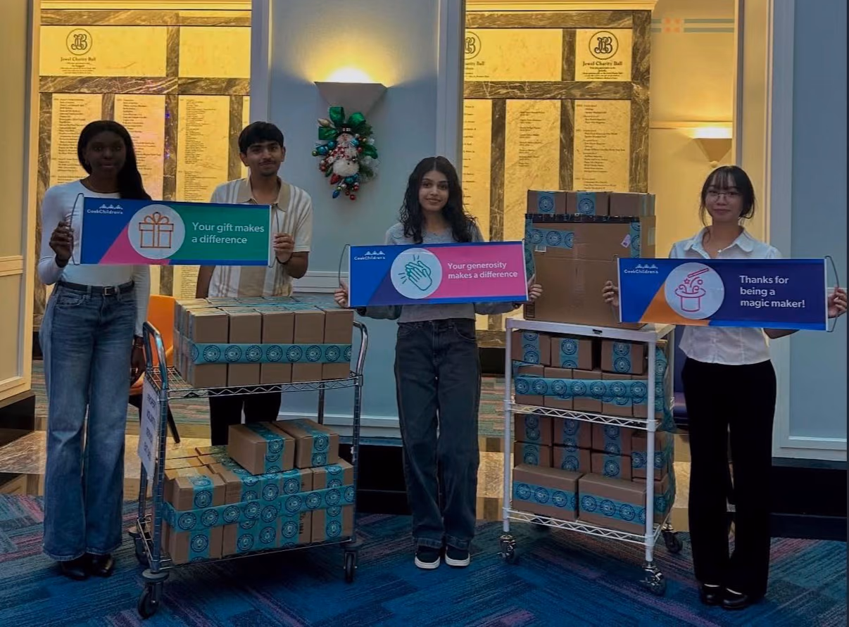 Four chapter members holding Cook Children's thank-you signs beside carts of STEMKits