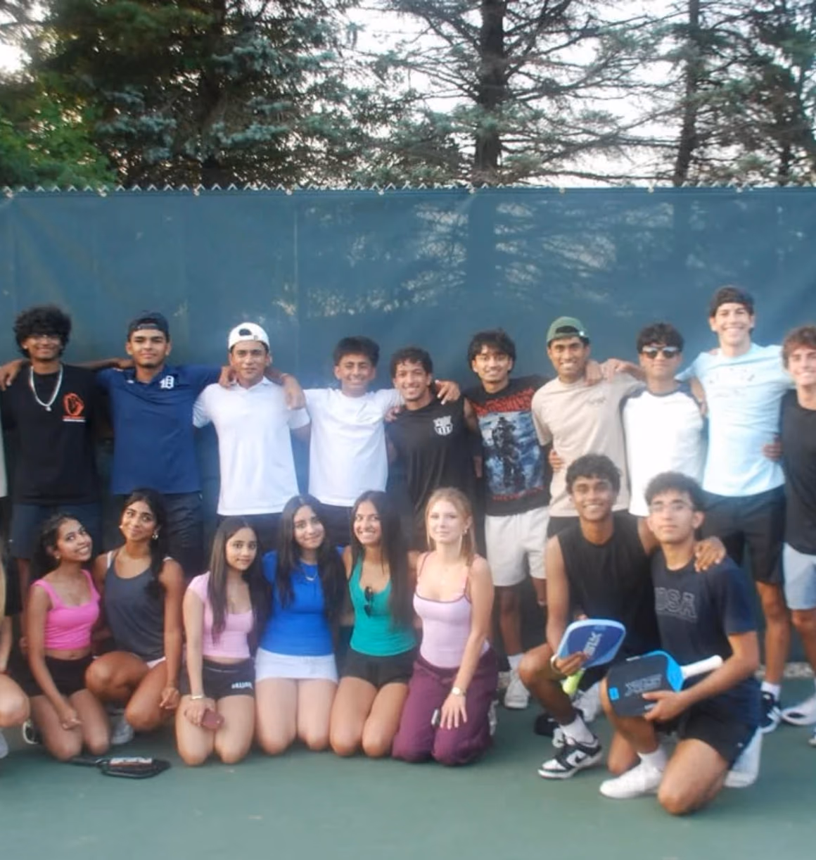 A large group of players and volunteers posing together on the pickleball court