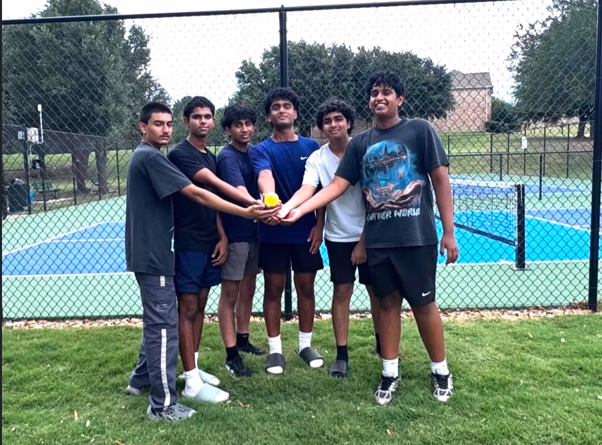 Six players stacking hands over a pickleball in front of the courts