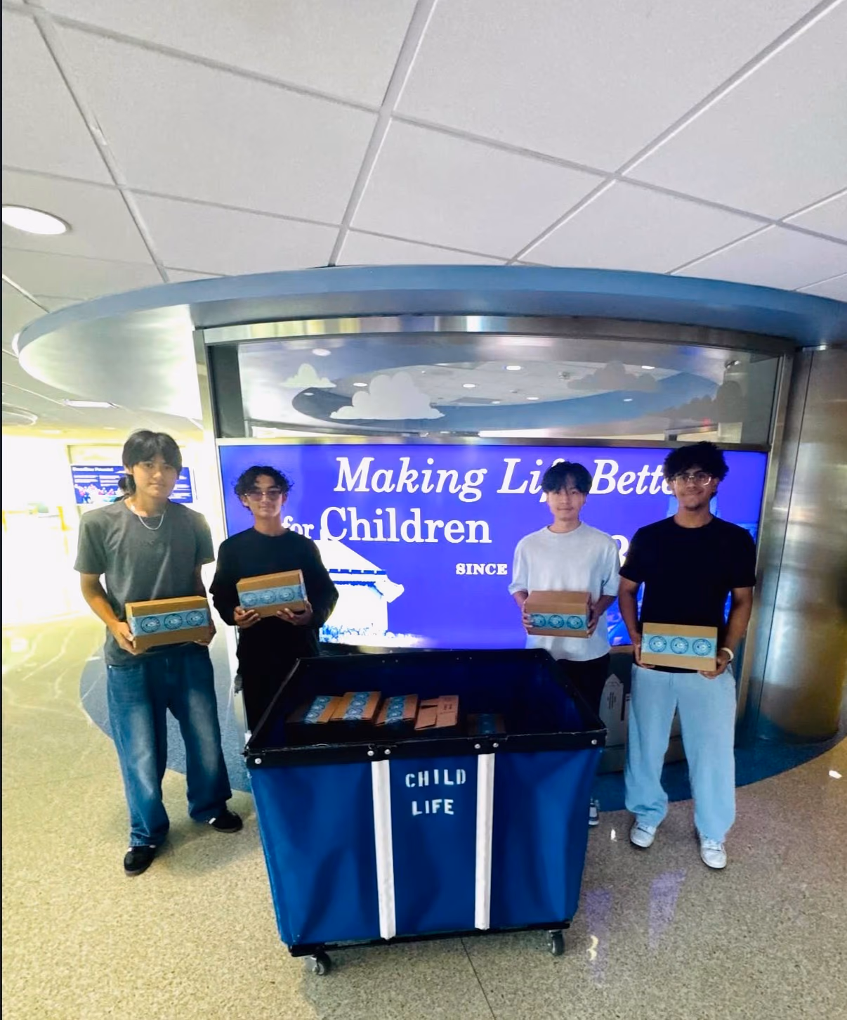 Four chapter members holding STEMKits beside a Child Life cart inside Children's Medical Center Dallas